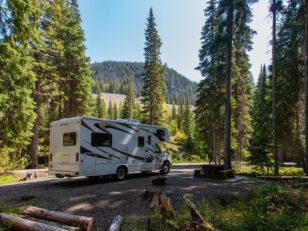 Beautiful campsite in the mountains with an RV and wooden bench.